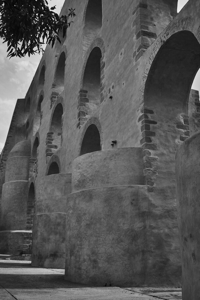 Ancient stone structure with multiple arches and weathered cylindrical columns in black and white