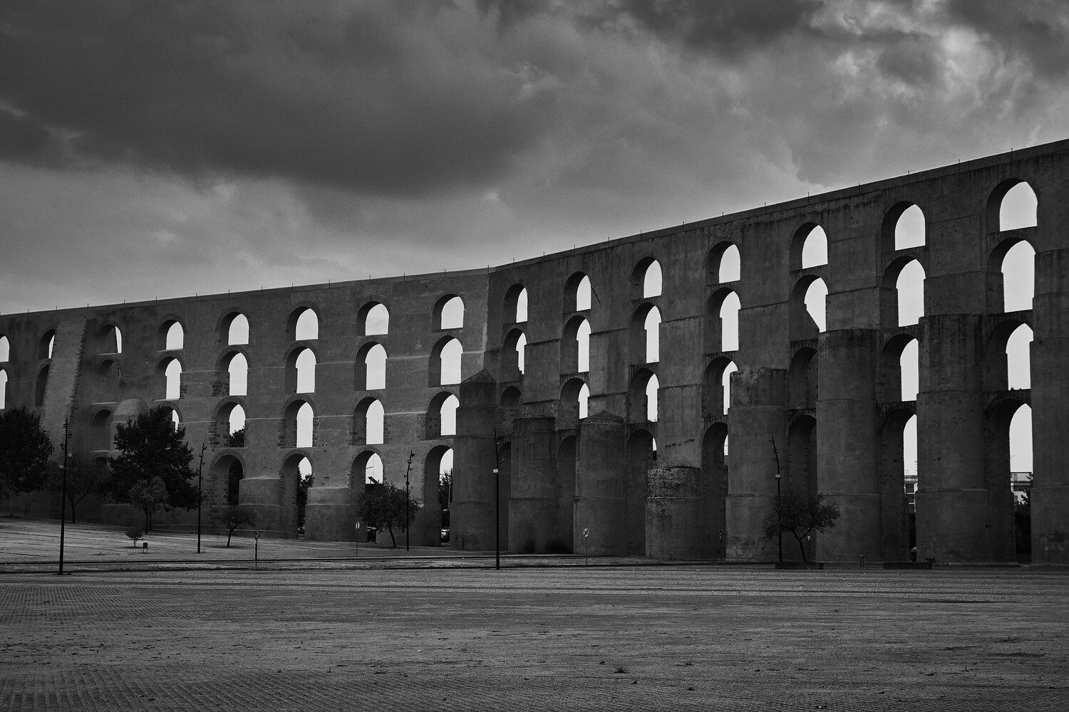 Black and white photograph of a massive ancient Roman aqueduct with repeating arched openings