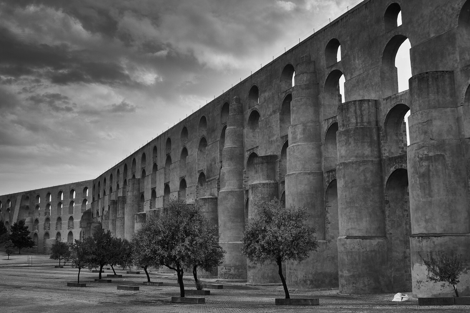 Ancient stone aqueduct with multiple arched openings and supporting columns in black and white