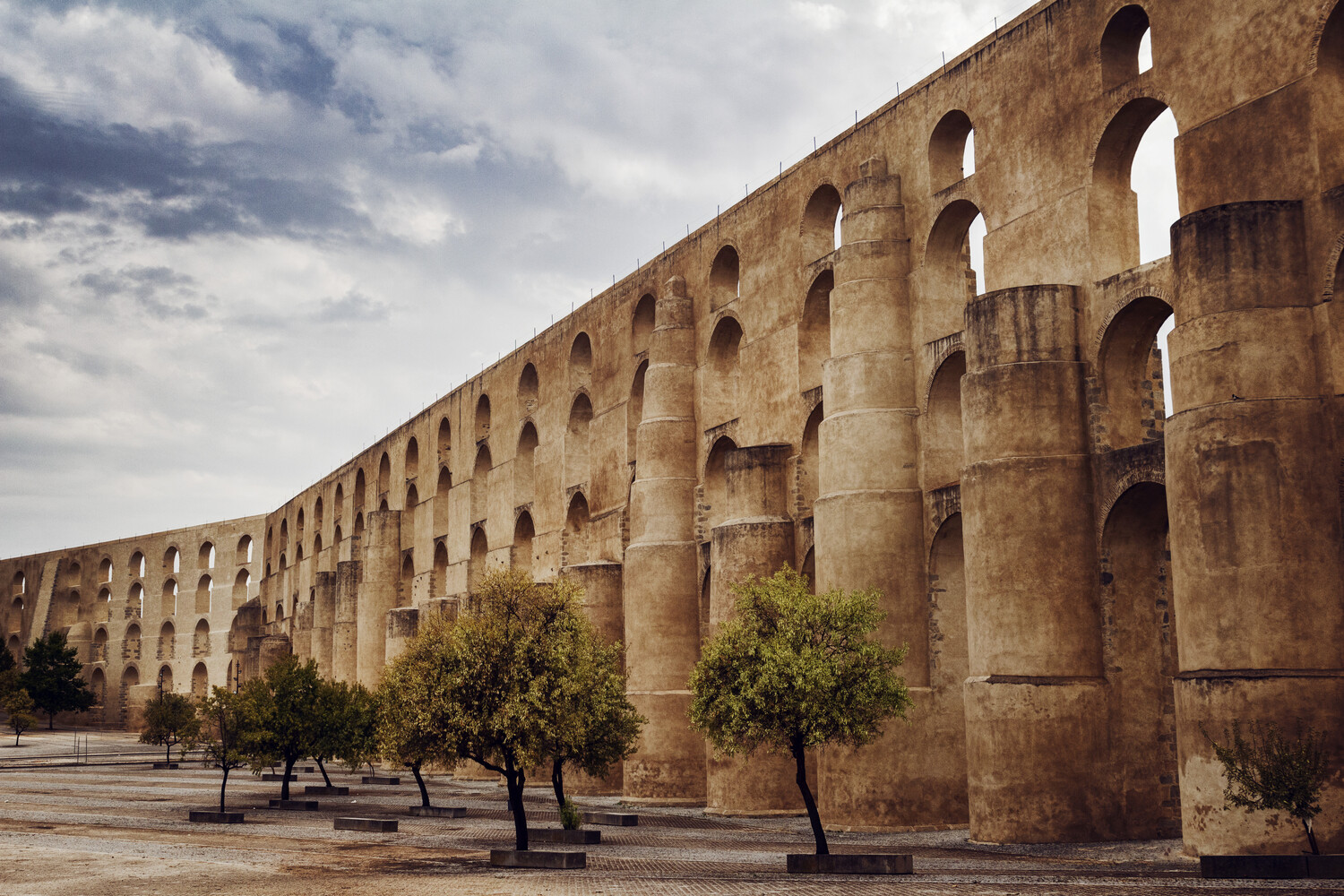 Ancient Roman aqueduct with multiple tiers of arches under dramatic cloudy sky