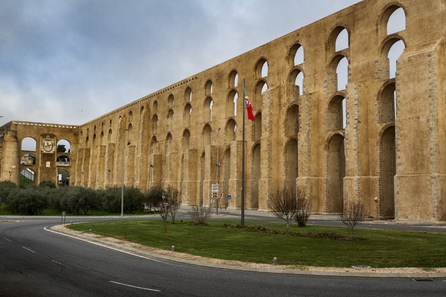 Ancient Roman aqueduct with multiple arches in golden stone, featuring a curved road and landscaping in foreground