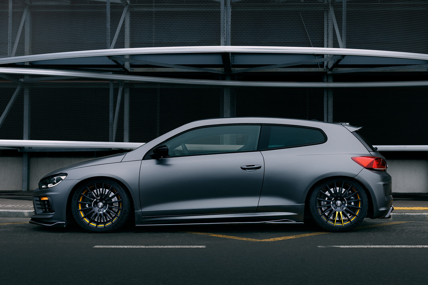 Silver performance hatchback photographed in profile against a modern parking structure with geometric steel framework