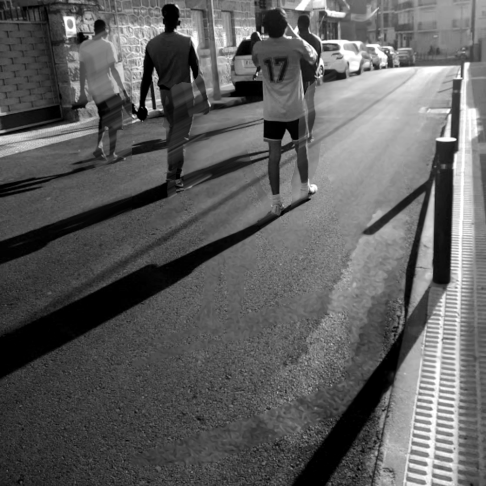 Pedestrians walking on a sunny urban sidewalk with strong shadows cast across the pavement