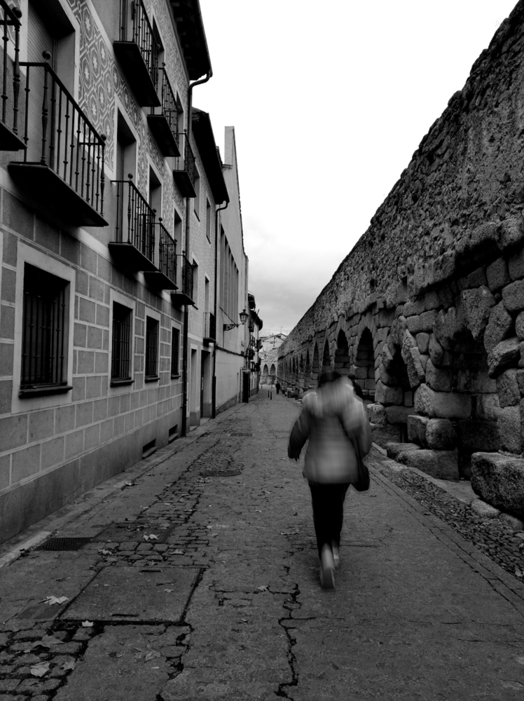 Figure running away down a narrow European cobblestone street lined with historic buildings