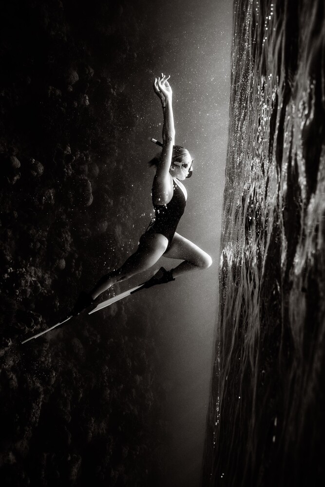 Shirtless male figure suspended horizontally against textured wall in dramatic monochrome lighting