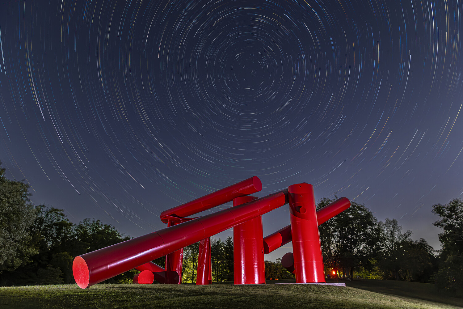 Illuminated red metal sculpture against star trail night sky