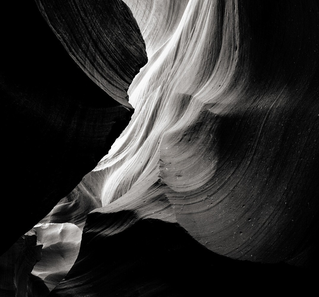 Abstract black and white photograph of curved rock formations with flowing, wave-like striations
