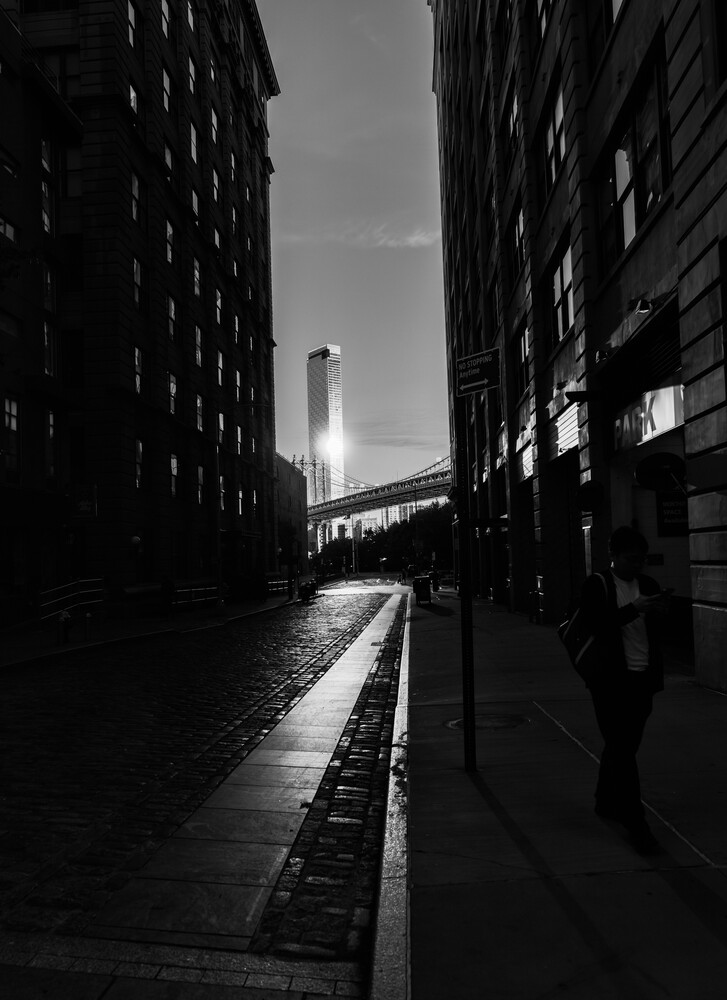 Narrow urban alley between tall buildings with distant skyscraper framed in center, wet pavement reflecting light