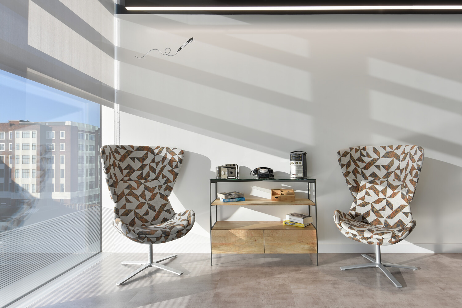 Modern interior with two patterned wingback chairs flanking a metal shelving unit near floor-to-ceiling windows