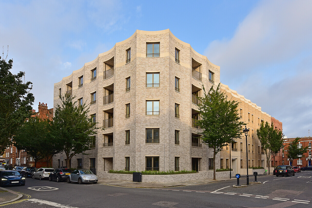 Modern residential building with honey-colored stone facade and angular roofline on urban street corner