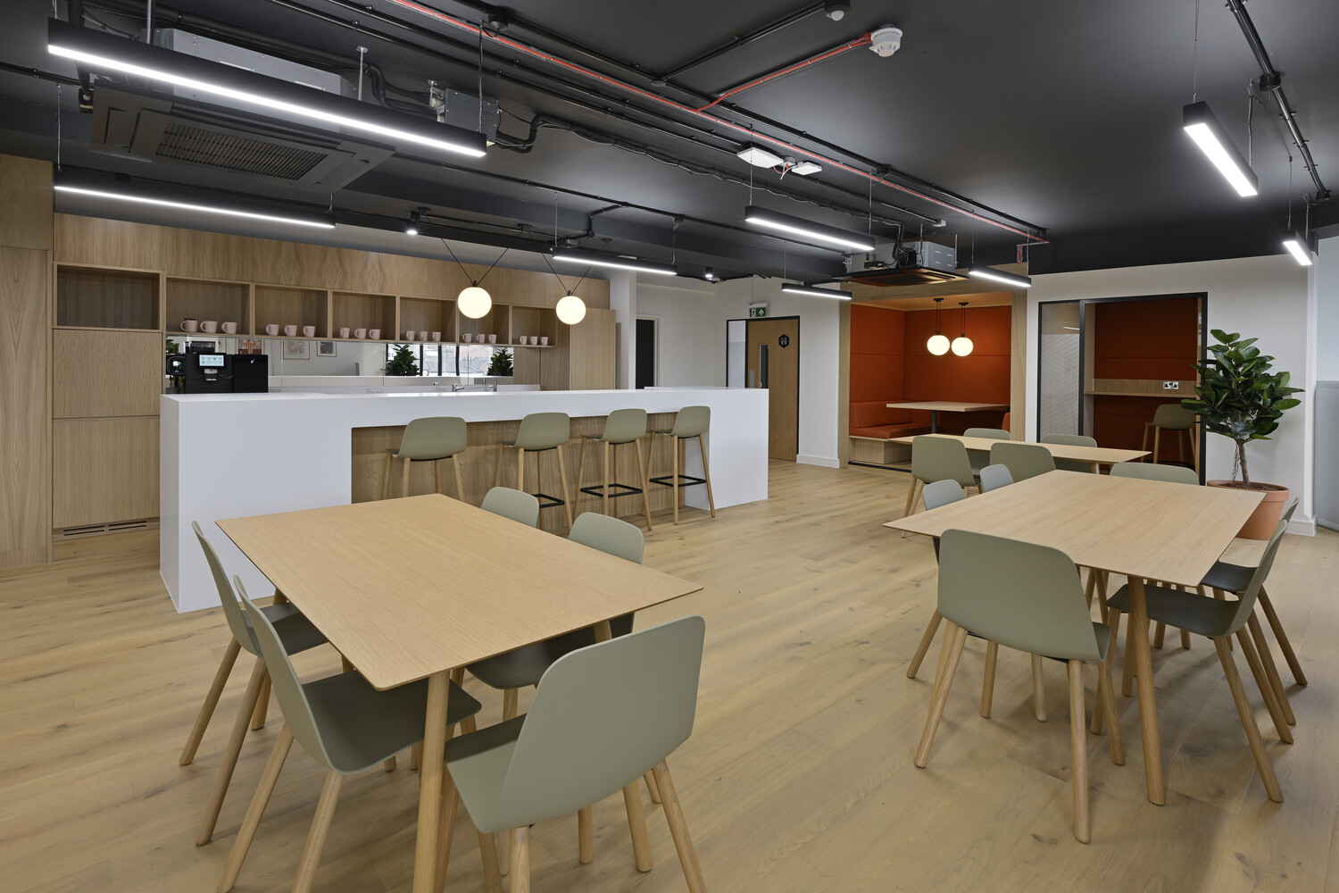 Modern office break room with wooden tables, light green chairs, and a central counter with bar seating