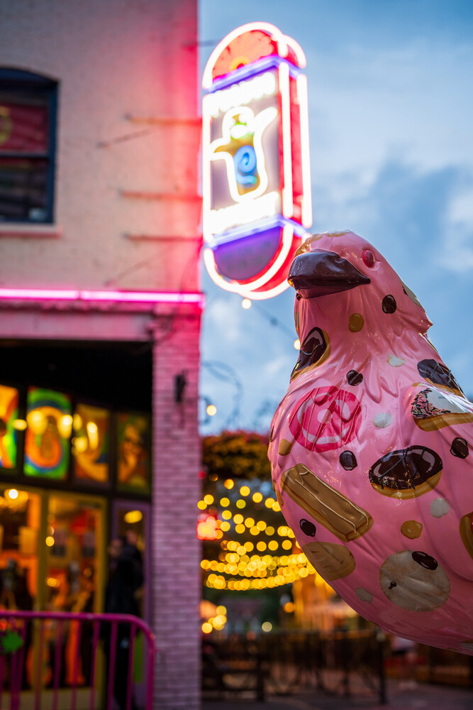 Pink retro vending machine with neon sign glowing against blue twilight sky and urban storefront