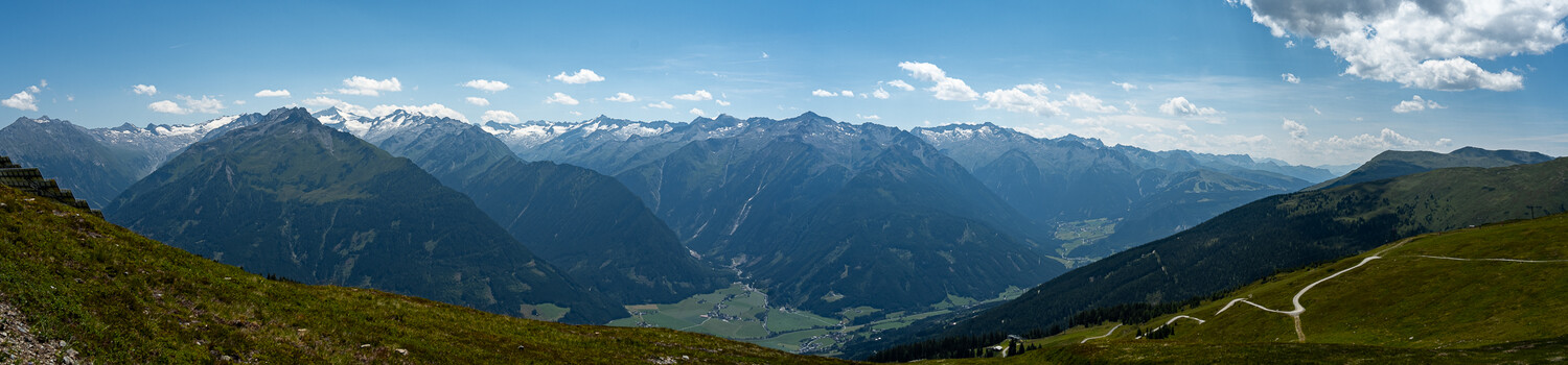 Alpine valley landscape with snow-capped mountains, green meadows, and winding road
