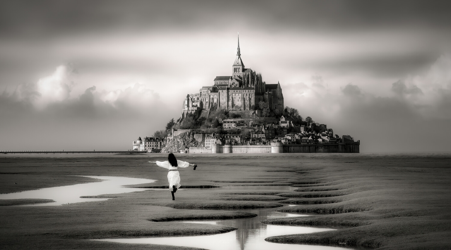 Solitary figure in waders walking through tidal flats toward Mont-Saint-Michel