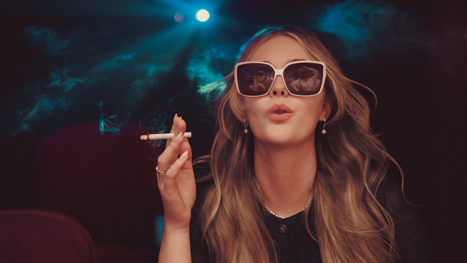 Woman wearing oversized sunglasses and smoking a cigarette against a nighttime sky with moon