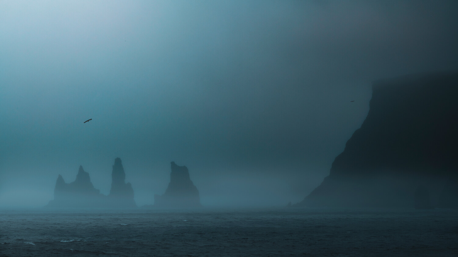 Misty seascape with silhouetted rock formations emerging from fog and dark water