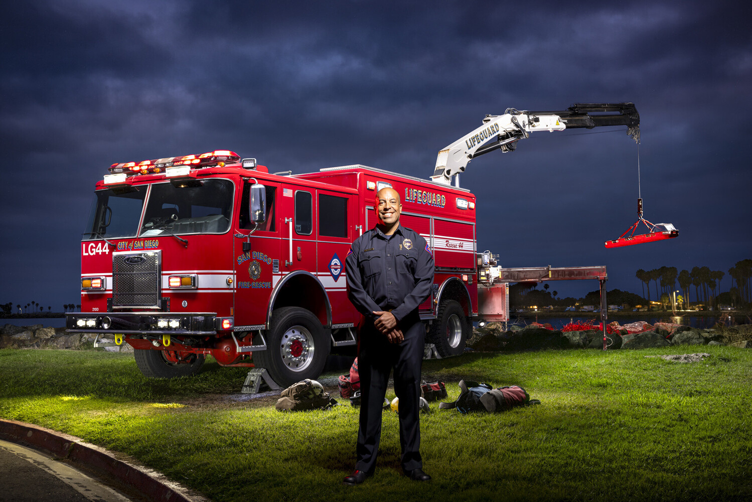 Firefighter standing in front of red fire truck with extended aerial ladder against dramatic storm clouds