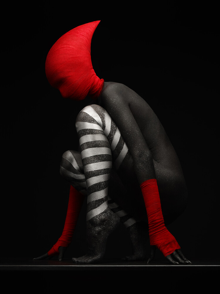 Silhouetted figure in dramatic red and black costume with skeletal chest striping against dark background