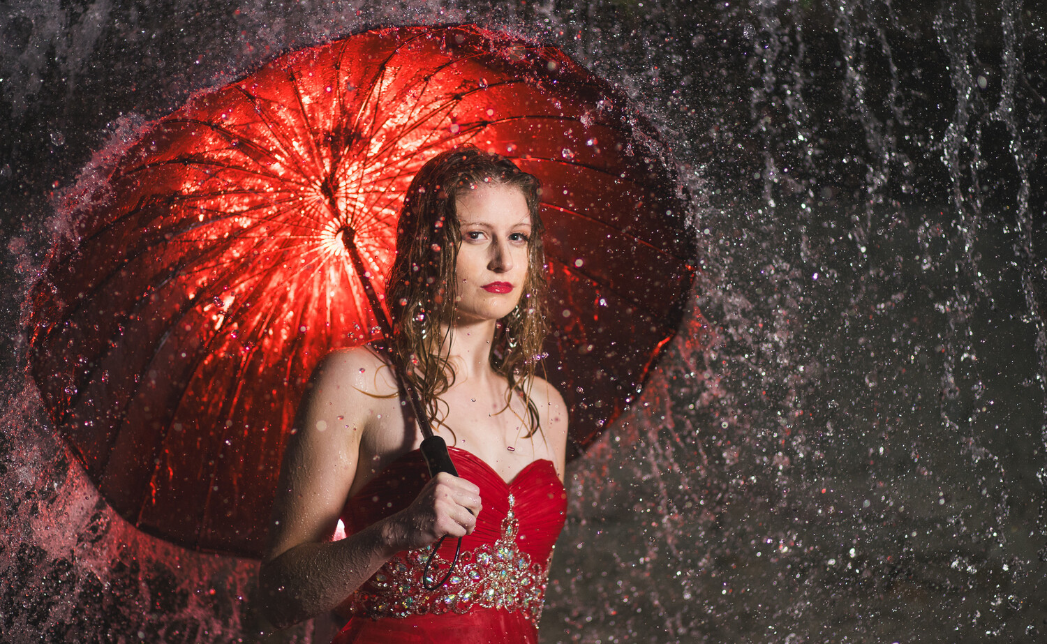 Woman in red dress holding red umbrella in falling rain and snow