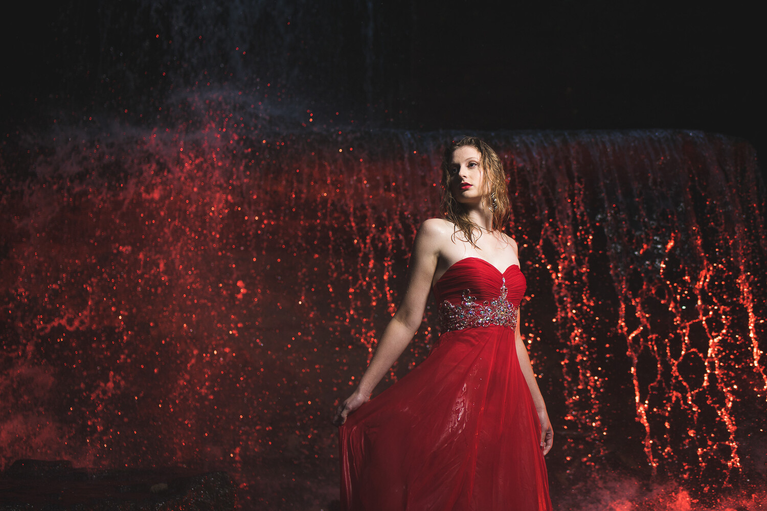 Woman in red sweetheart gown against glowing red particle backdrop
