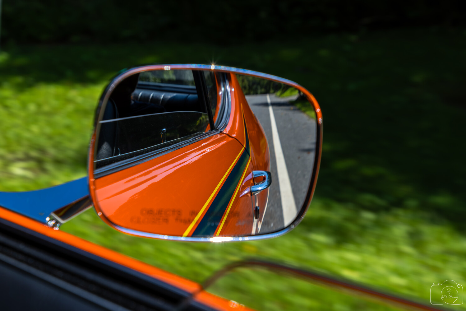 Orange and blue vintage car reflected in its side mirror with green foliage background