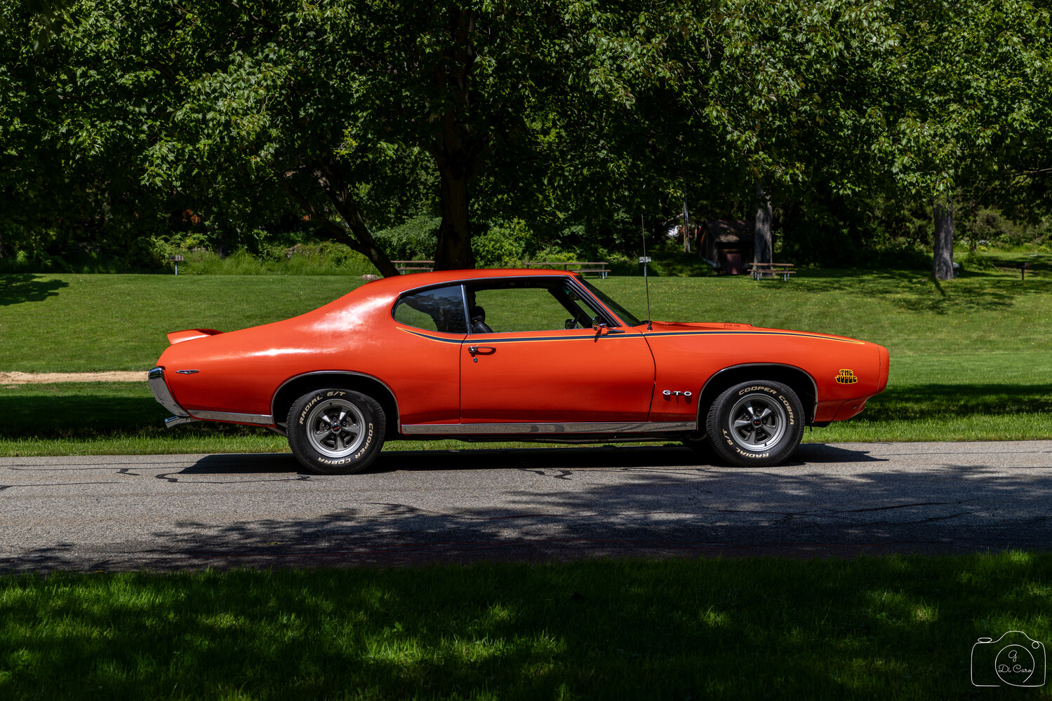 Bright orange muscle car parked on tree-lined street with green lawn in background