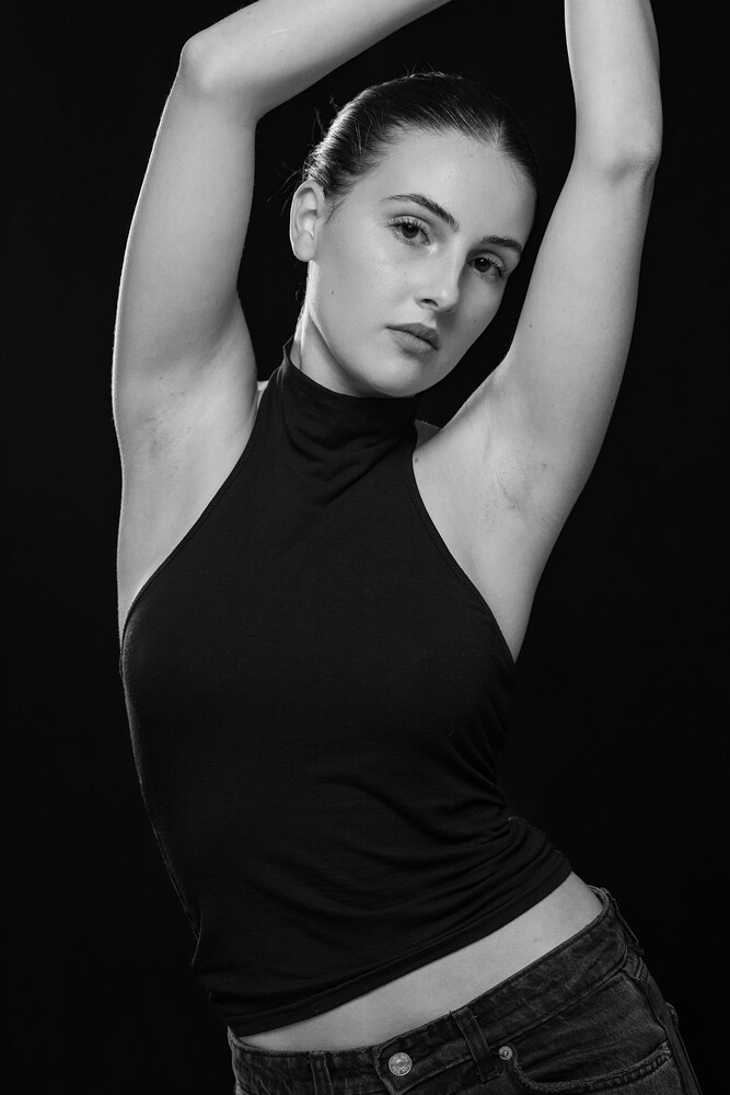 Woman in black sleeveless top with arms raised overhead against dark background