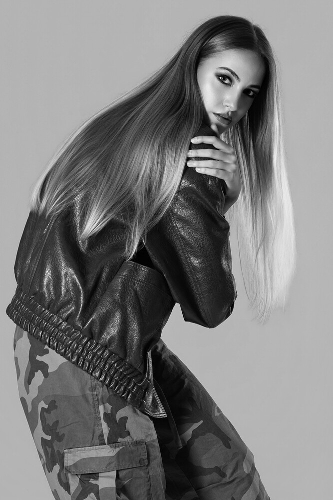 Woman with long straight hair in black leather jacket, hand raised to face, studio portrait