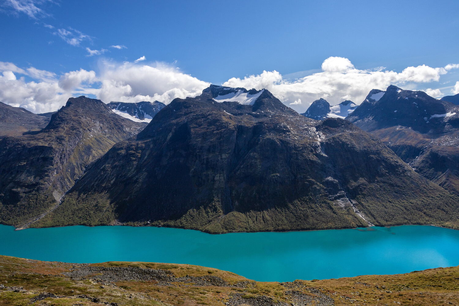 Turquoise alpine lake surrounded by dramatic mountain peaks under blue sky with clouds