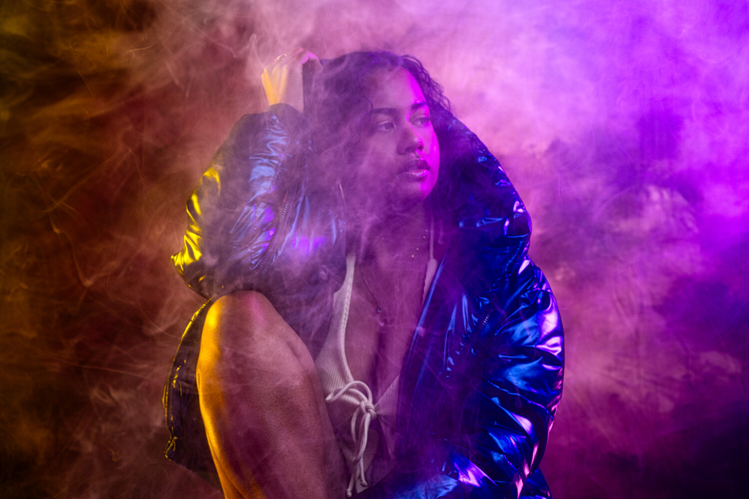 Woman in metallic jacket surrounded by vibrant purple and golden smoke