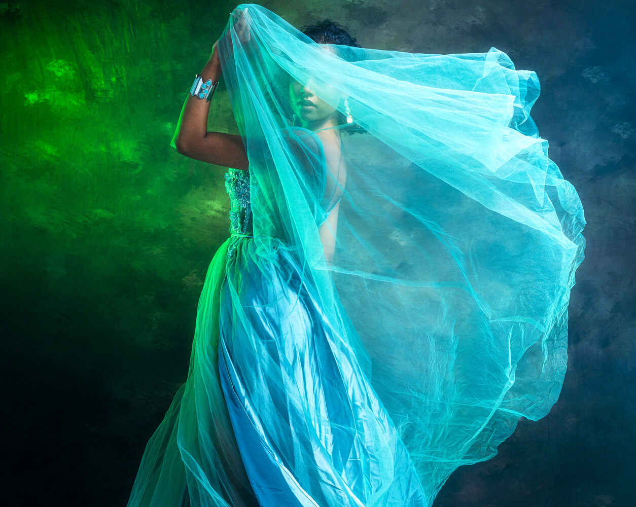 Person silhouetted behind billowing turquoise tulle fabric against green and dark blue lighting