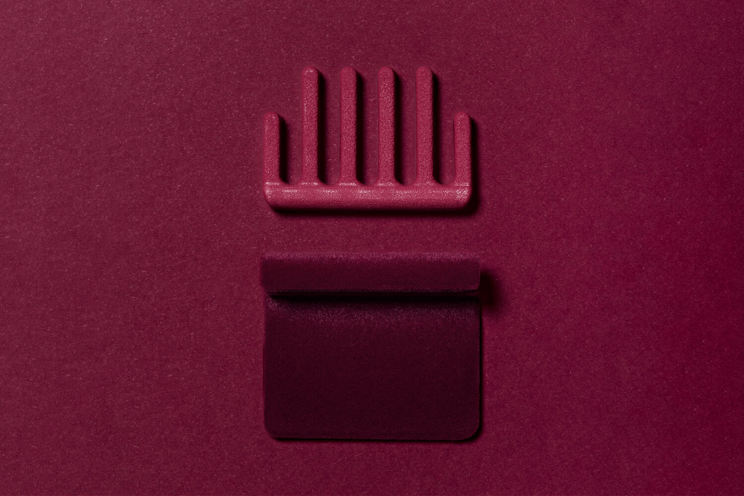 Monochromatic still life composition featuring a comb and rectangular object on burgundy surface