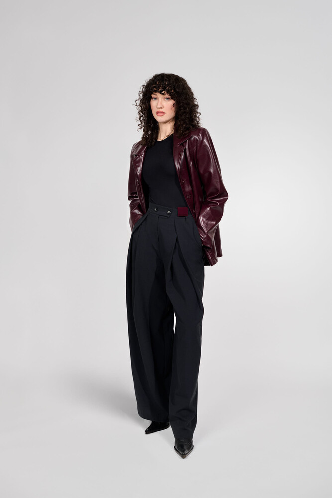 Woman in black outfit with burgundy velvet blazer standing against neutral background