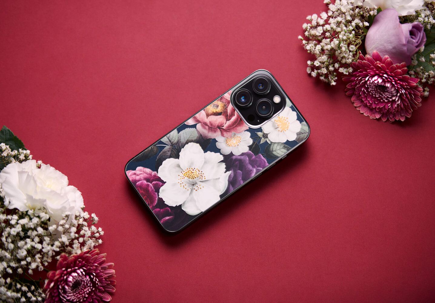 Smartphone with floral case design positioned on magenta background surrounded by fresh flowers