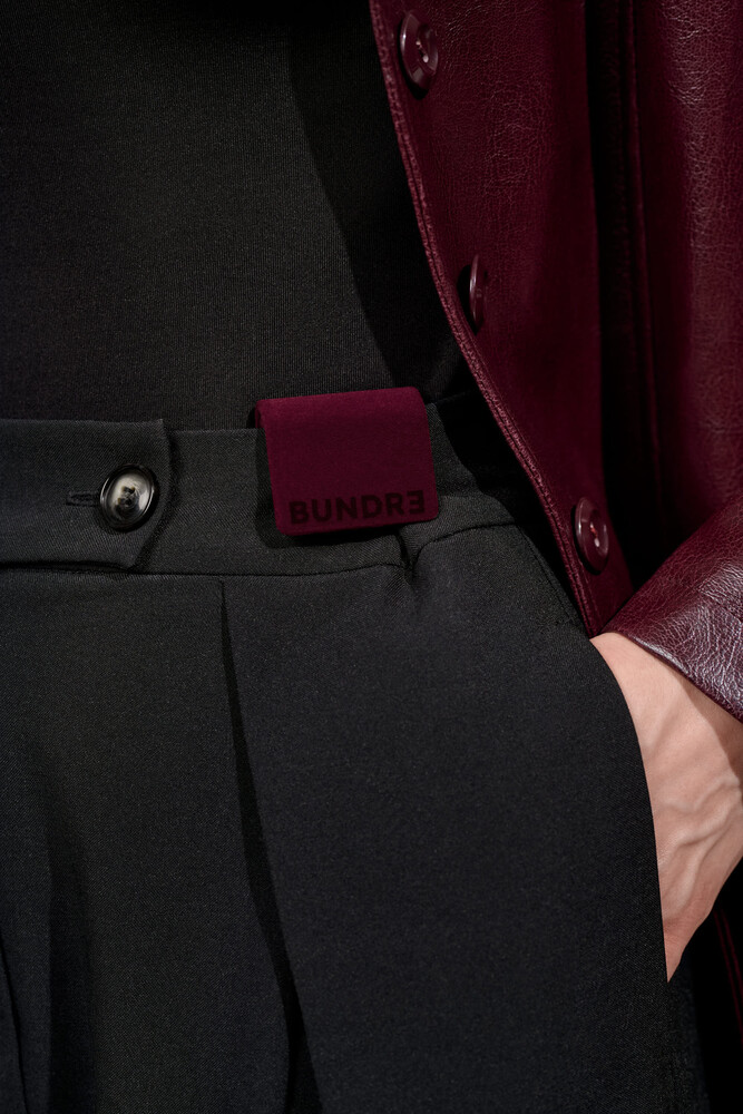 Close-up of black trousers with burgundy pocket detail and fabric drape