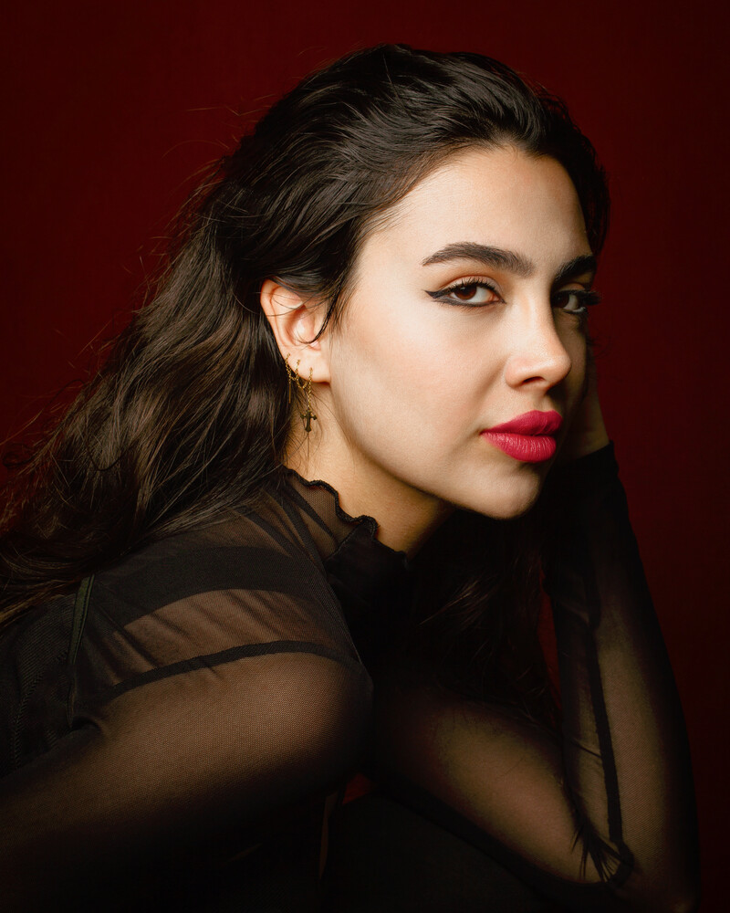 Woman with long dark hair wearing black clothing against deep red background