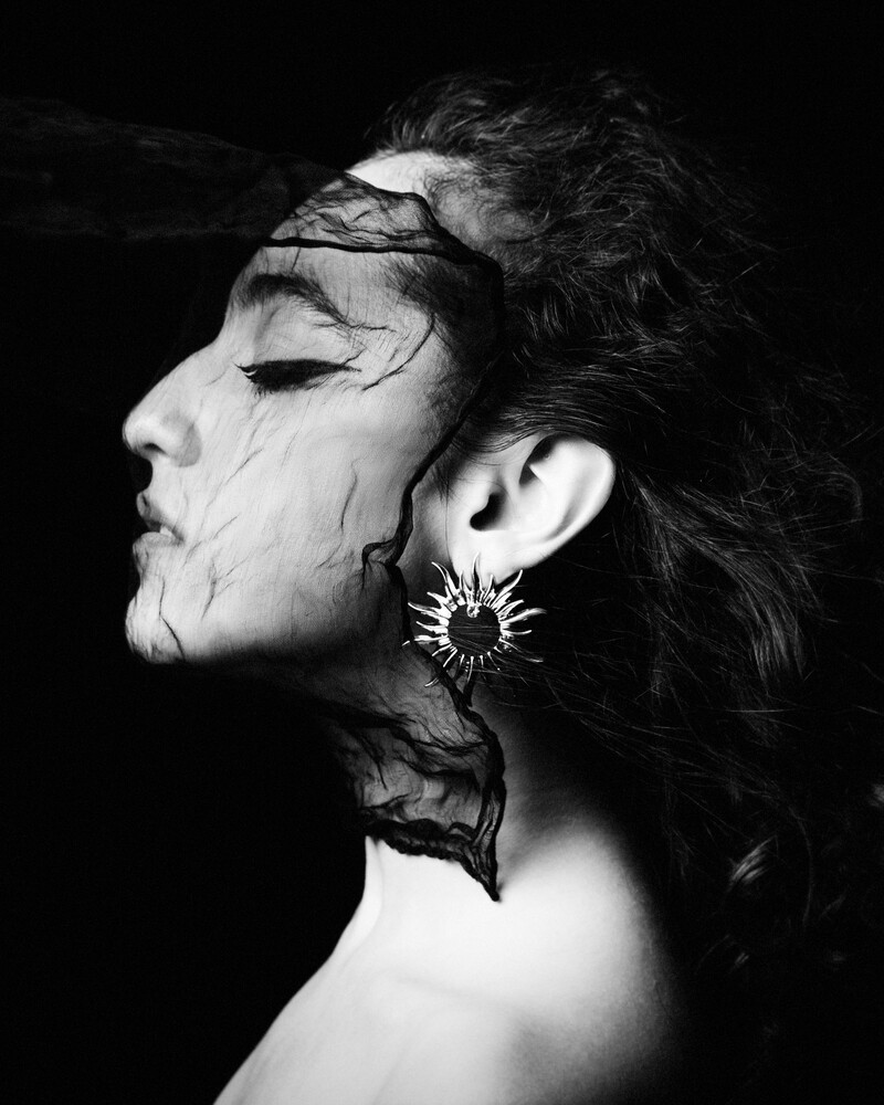Profile of person with dramatic face paint and spiked earring against black background