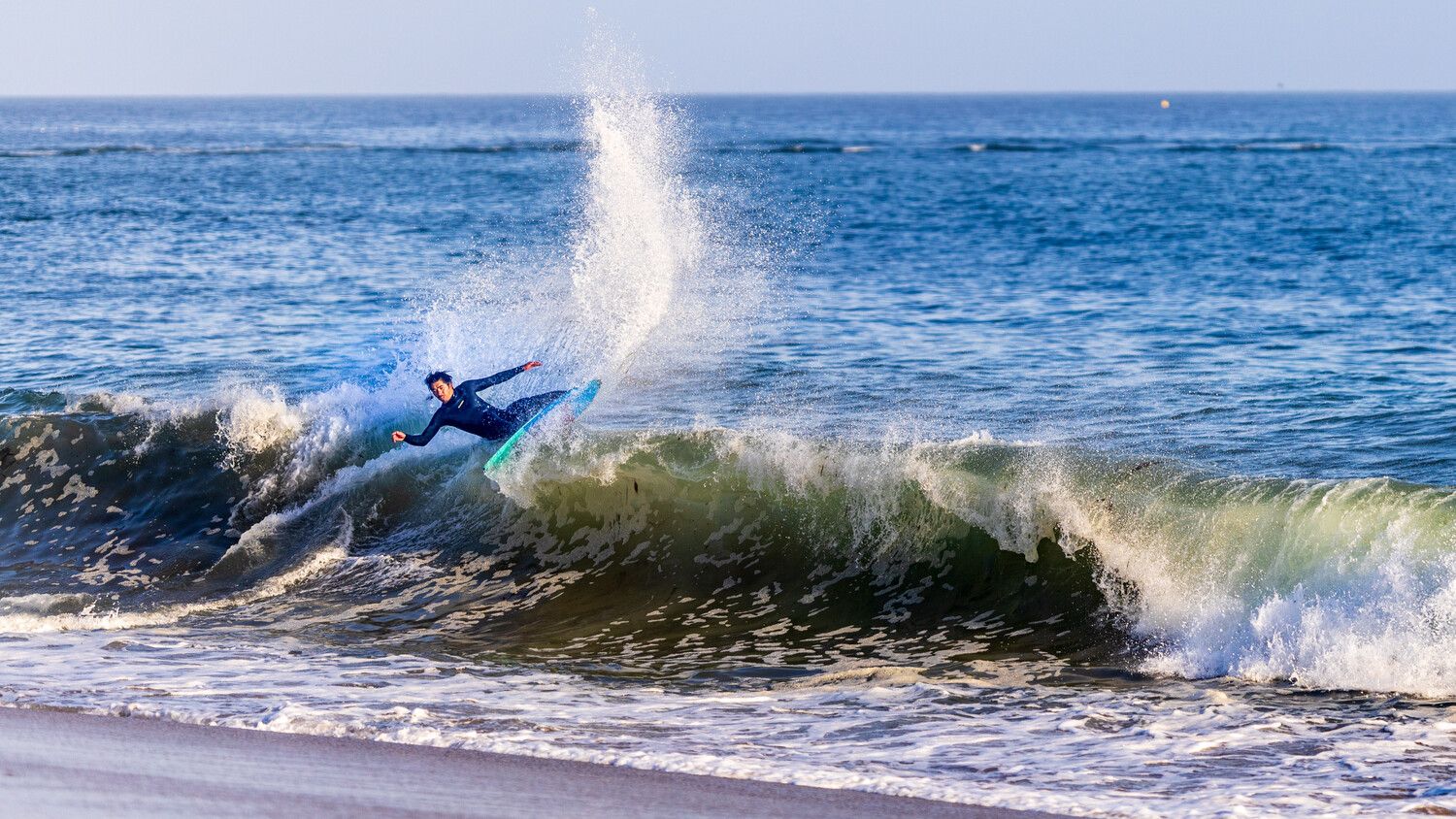 Surfer in blue wetsuit riding a wave with spray and whitewash