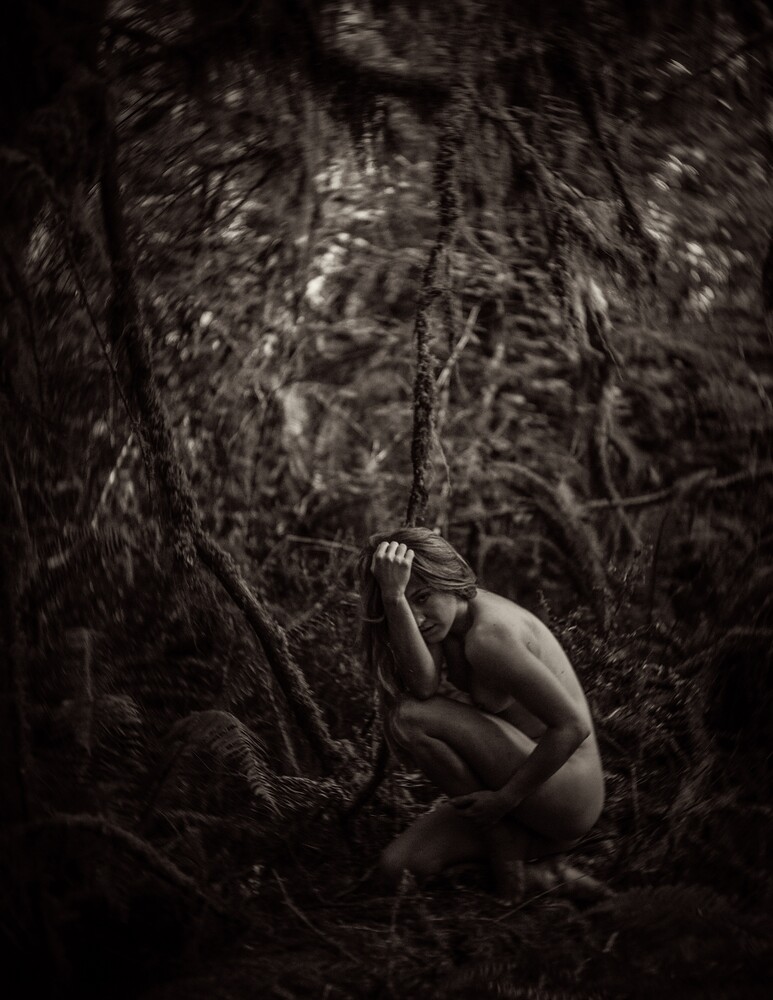Sepia-toned fine-art photo of a bare-backed figure crouched among ferns and tangled roots in a dark forest.