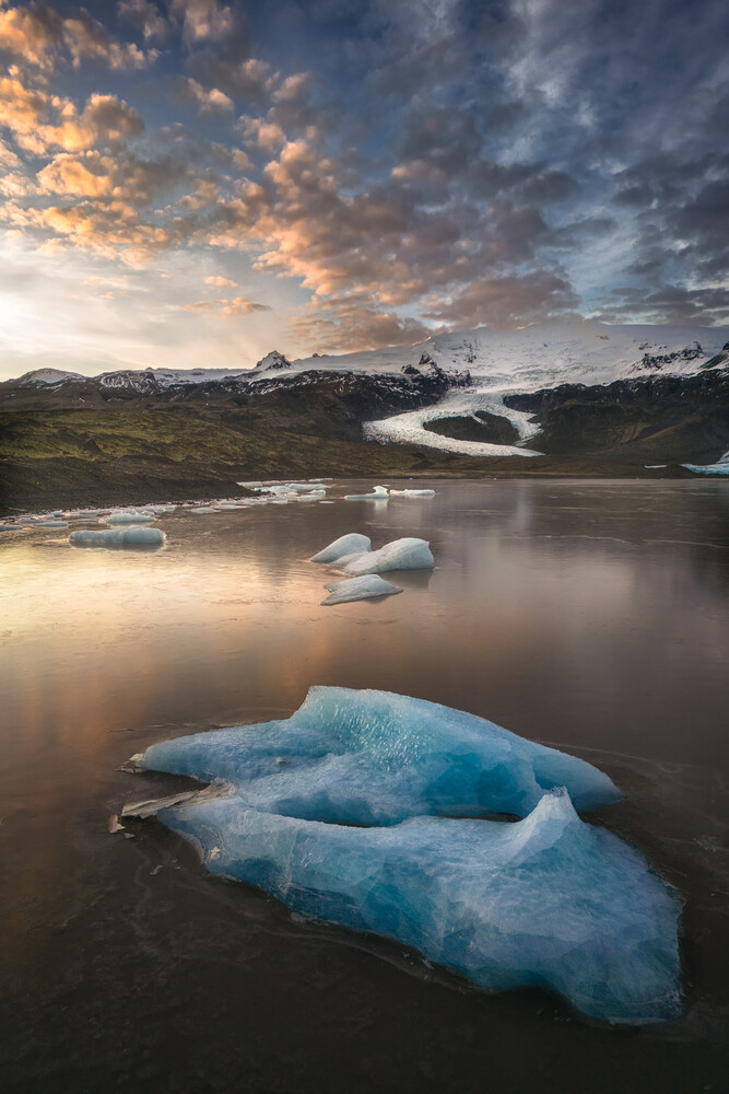 Luminous blue icebergs floating in glacial lagoon beneath dramatic dawn sky