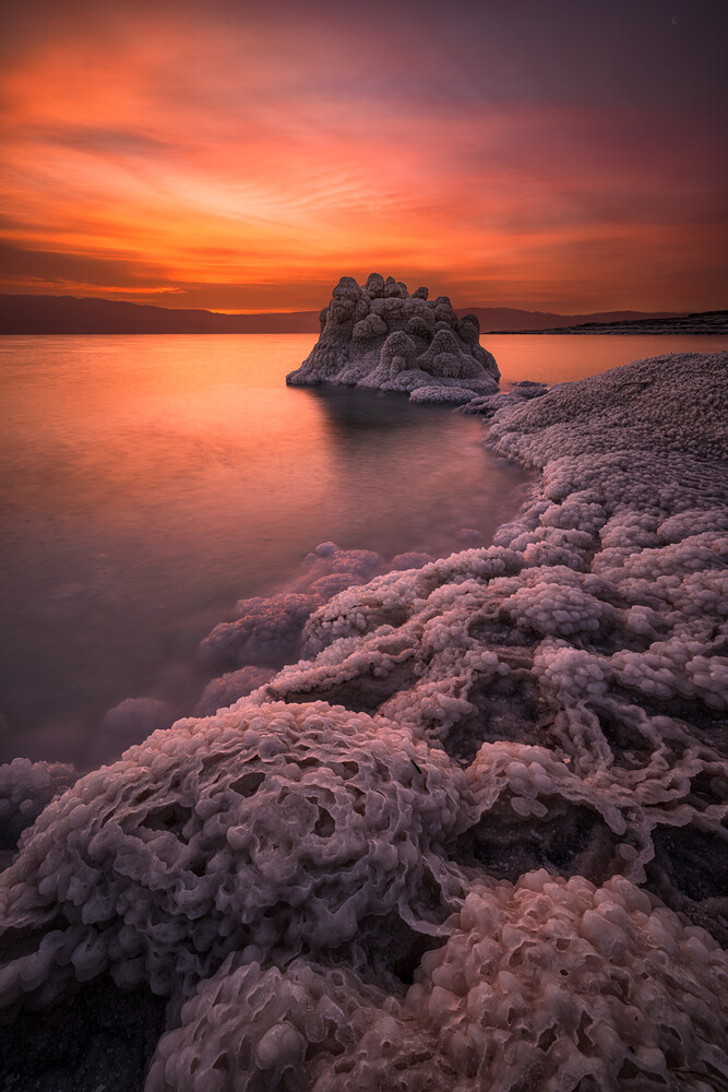 Rocky outcrop silhouetted against dramatic orange and purple sunset over calm water
