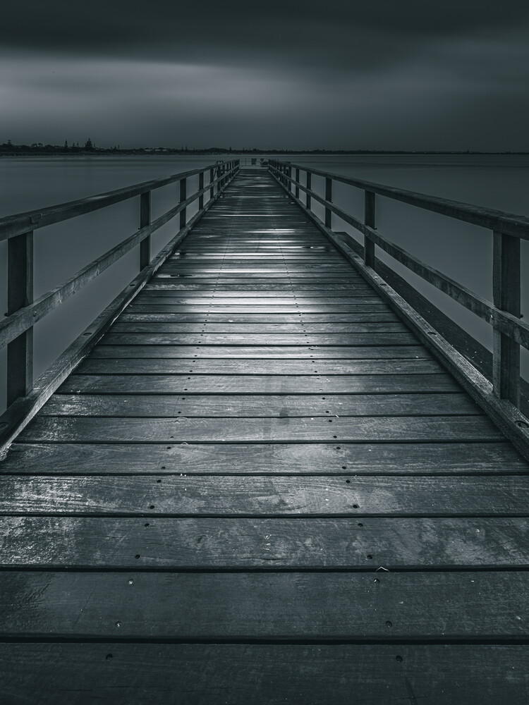 Wooden boardwalk extending into moody gray water under overcast sky