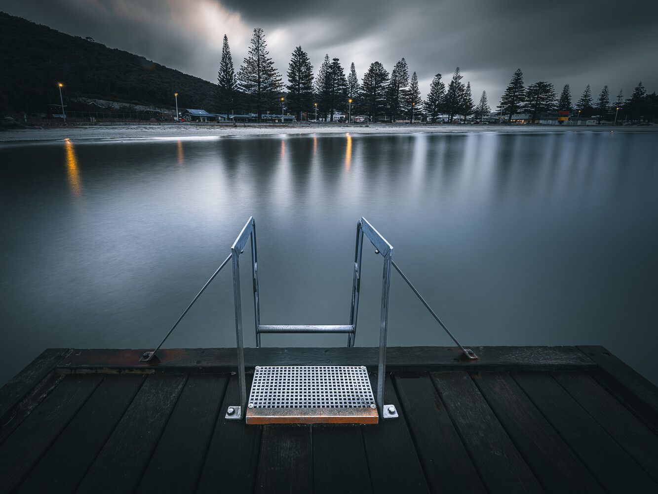 Wooden dock with metal railings extending into a still, misty lake surrounded by evergreen trees
