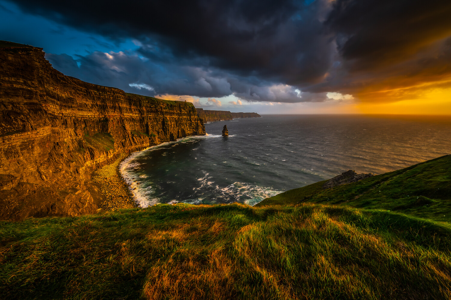 Dramatic coastal cliffs at sunset with golden light illuminating layered rock formations and a solitary sea stack