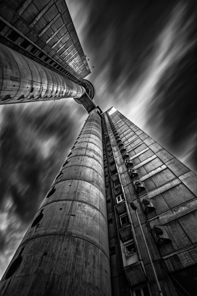 Upward perspective of cylindrical towers converging toward sky with dramatic clouds
