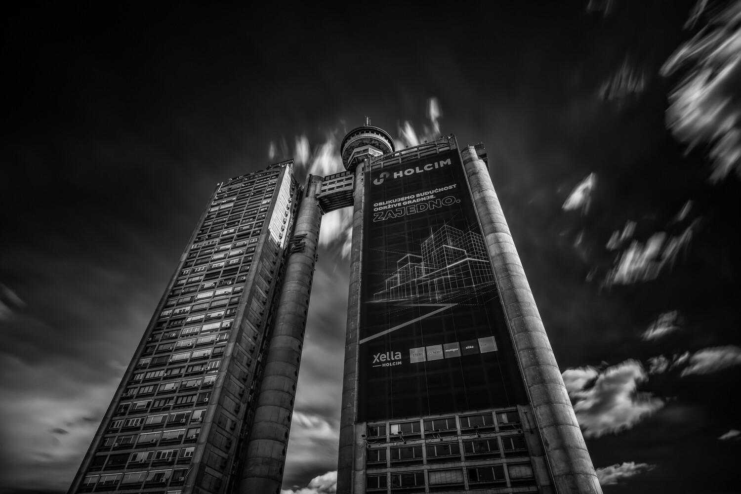 Modern cylindrical high-rise building shot from below against dramatic cloudy sky in black and white