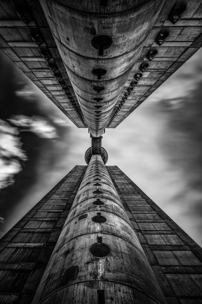 Symmetrical upward view of a tall cylindrical structure with repetitive architectural elements against dramatic sky