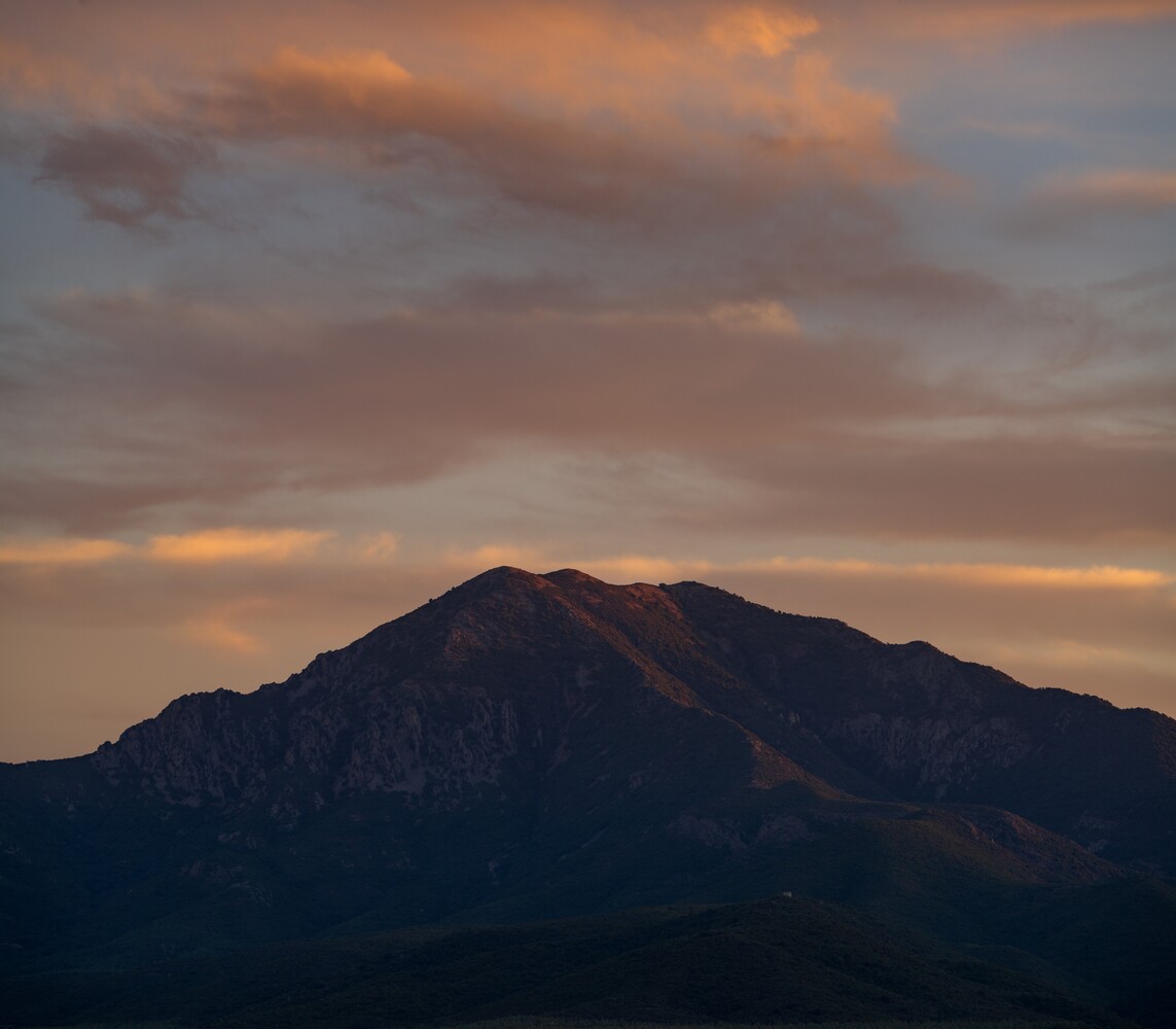 Silhouetted mountain peak beneath dramatic golden-hour sky with layered clouds