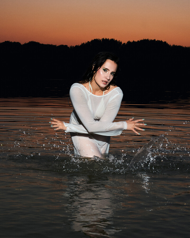 Woman in white long-sleeve shirt in water at dusk with arms outstretched
