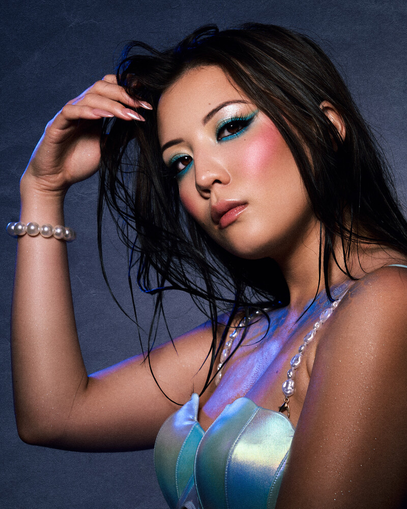 Portrait of a woman with long dark hair wearing blue headphones around her neck against a blue gradient background